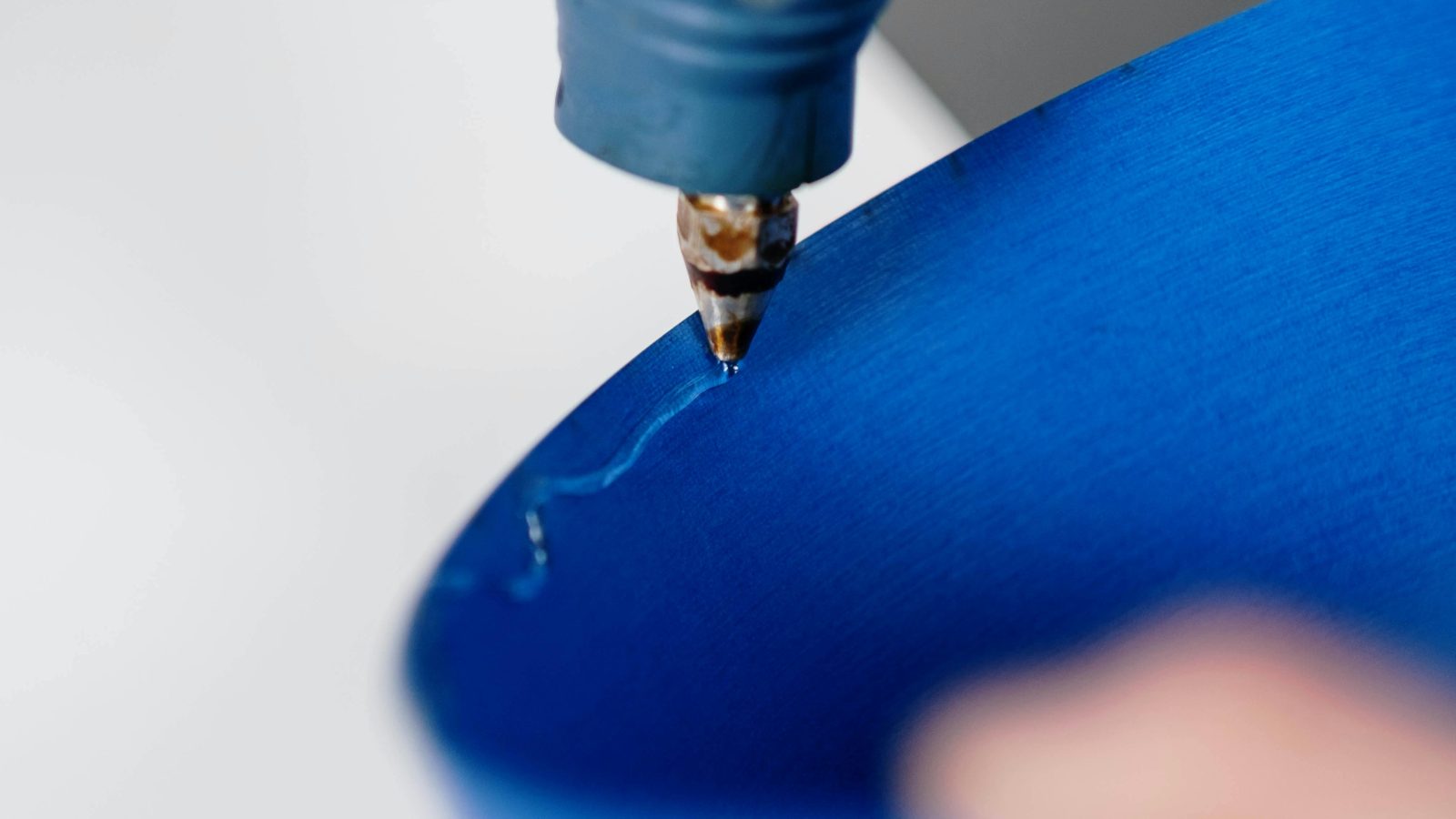 Close-up of a glue gun applying hot glue on blue paper with depth of field effect.